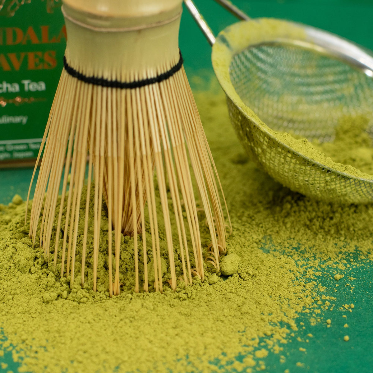 Traditioneller Matcha-Besen und Sieb mit leuchtend grünem Matcha-Pulver auf einer Oberfläche.
